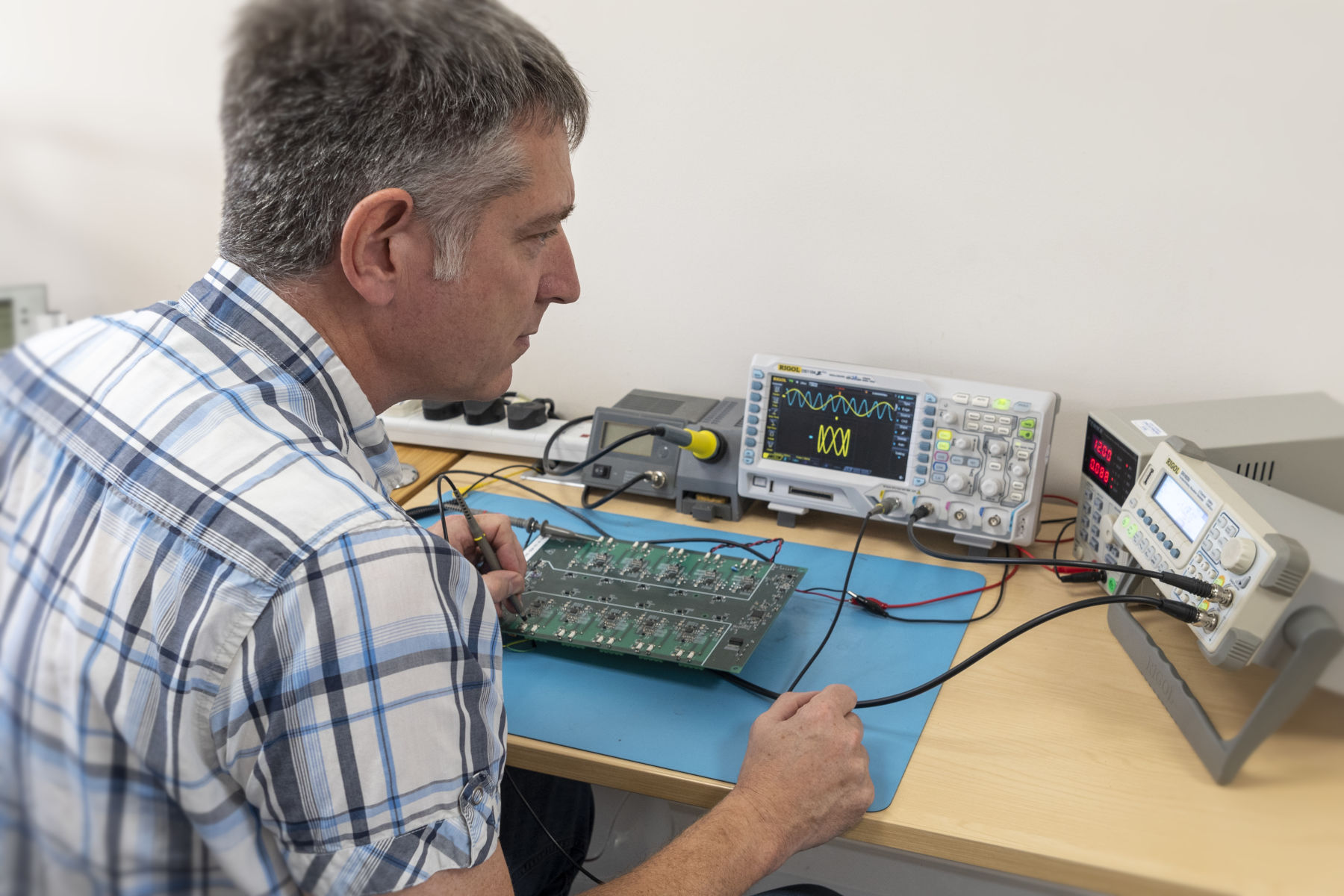 Electronic engineer with PCB, oscilloscope and function generator