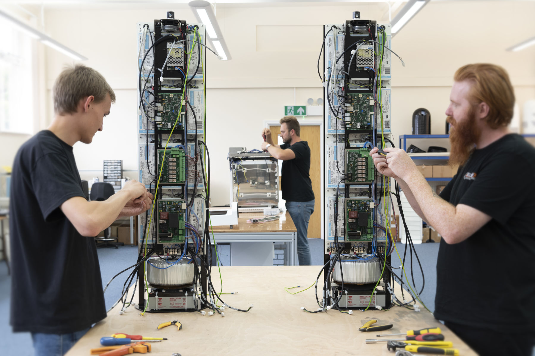 Technicians assembling PCBs and wiring into tall mechanical assembly