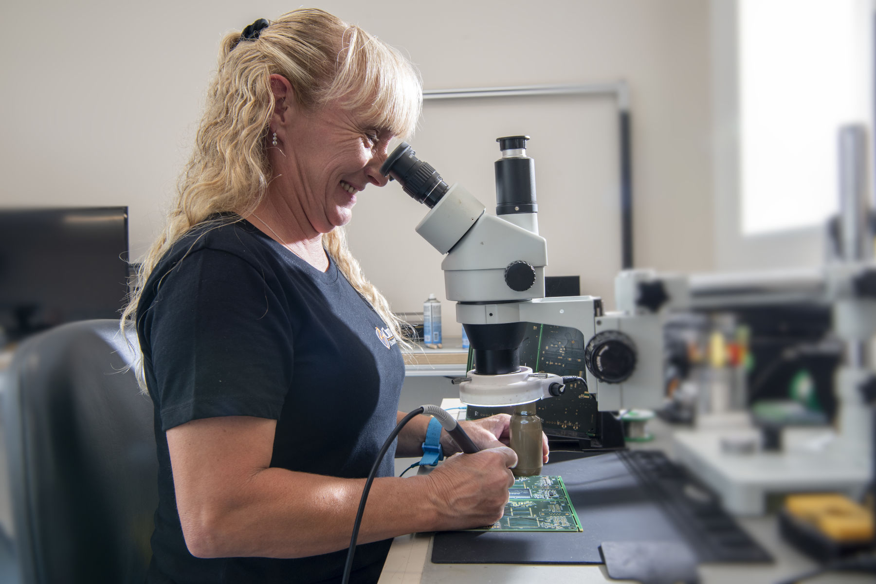 Electronics technician using microscope while hand soldering surface mount components onto a PCB assembly