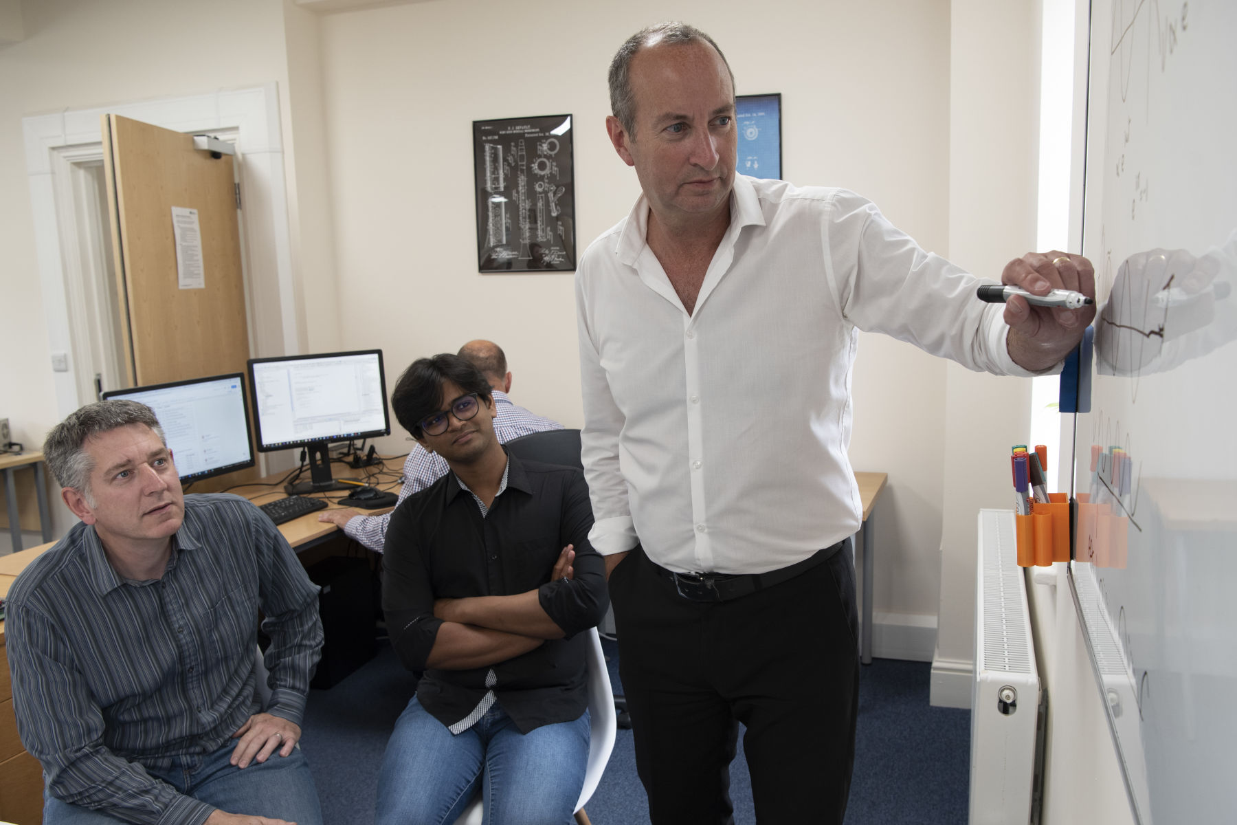 Engineers discussing electronic circuit design around a whiteboard